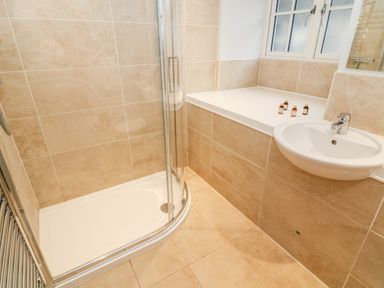 A bathroom with a corner shower enclosure a wall-mounted sink and bottles on a ledge by a window at Lowe-McConnell in Far Sawrey