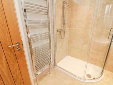 A bathroom with a glass shower enclosure and a chrome towel radiator next to a wooden door at Lowe-McConnell in Far Sawrey