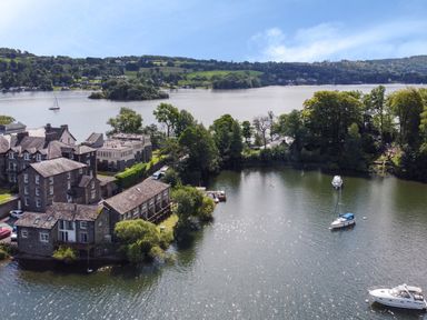 A waterfront area with boats docked near residential buildings and trees at Lowe-McConnell in Far Sawrey