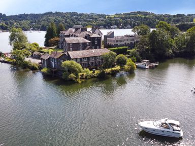 A waterfront property with boats on a lake surrounded by trees at Lowe-McConnell in Far Sawrey