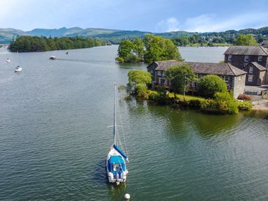A lake with sailboats and stone buildings surrounded by trees at Lowe-McConnell in Far Sawrey