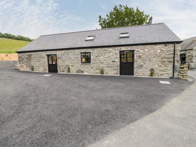 A stone building with two black doors and two windows on a paved area at The Shippon in Llanrwst