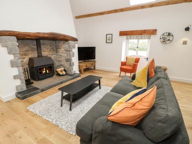 A living room with a stone fireplace a gray sofa with colorful cushions an orange armchair a black coffee table and a television at The Shippon in Llanrwst