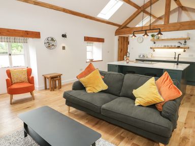 A living room with a gray sofa and colorful cushions next to an orange armchair and a kitchen with island and shelves at The Shippon in Llanrwst