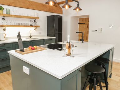 A kitchen with a central island, black stools, and wooden shelves with glasses and mugs at The Shippon in Llanrwst