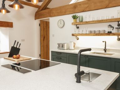 A kitchen with a white countertop black faucet stove and wooden shelves with glasses and cups at The Shippon in Llanrwst