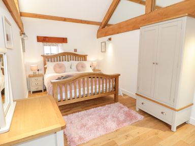 A bedroom with a wooden bed frame pink cushions two bedside tables with lamps a wardrobe a dresser and a pink rug at The Shippon in Llanrwst