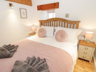 A bedroom with a wooden bed frame pink cushions and bedside tables with lamps at The Shippon in Llanrwst