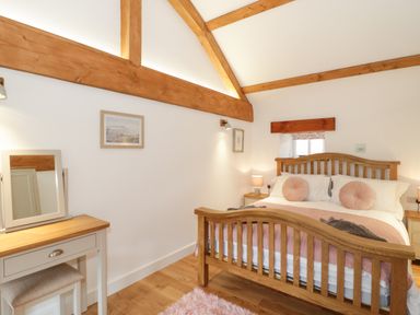 A bedroom with a wooden bed frame a dressing table with mirror and exposed wooden beams at The Shippon in Llanrwst