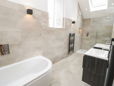 A bathroom with a bathtub shower area double sinks and a towel radiator at The Shippon in Llanrwst