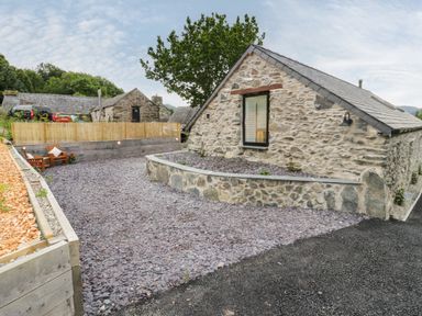 An outdoor area with a gravel driveway wooden fence and stone buildings at The Shippon in Llanrwst