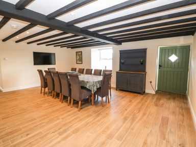 A dining room with a long table surrounded by chairs a television mounted on the wall a cabinet and a green door at Trewen in Botwnnog near Sarn Meyllteyrn