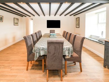 A dining room with a long table and twelve chairs under a ceiling with exposed wooden beams at Trewen Botwnnog near Sarn Meyllteyrn