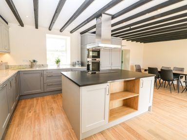 A kitchen with a central island, gray cabinets, a dining table with chairs, and exposed ceiling beams at Trewen in Botwnnog near Sarn Meyllteyrn