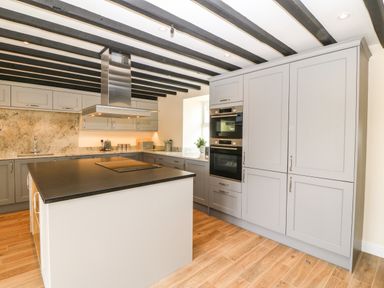 A kitchen with gray cabinets a central island with stovetop wooden floor and ceiling beams at Trewen in Botwnnog near Sarn Meyllteyrn