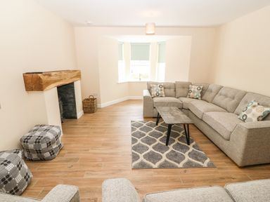 A living room with a gray sectional sofa a patterned rug a wooden mantel and a bay window at Trewen in Botwnnog near Sarn Meyllteyrn