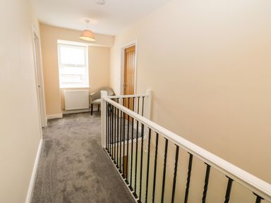 A hallway with grey carpet a window a radiator a chair and a wooden door at Trewen in Botwnnog near Sarn Meyllteyrn