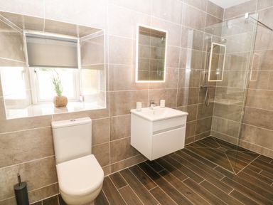 A bathroom with a toilet, a floating sink cabinet with a mirror above, a walk-in shower with glass partition, and a window with a plant on the sill at Trewen Botwnnog near Sarn Meyllteyrn