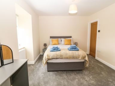 A bedroom with a bed with pillows and towels two bedside tables with lamps a wooden door and a dressing table with a mirror at Trewen in Botwnnog near Sarn Meyllteyrn