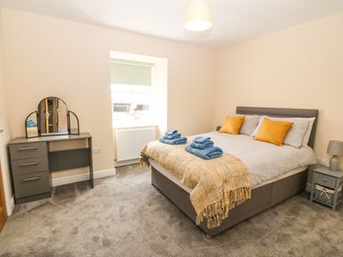 A bedroom with a double bed with pillows and folded towels a dressing table with a mirror and a bedside table with a lamp at Trewen Botwnnog near Sarn Meyllteyrn
