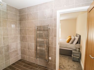 A bathroom with tiled walls and floor a metal towel rack and a view into a bedroom with a bed pillows and a bedside table at Trewen Botwnnog near Sarn Meyllteyrn