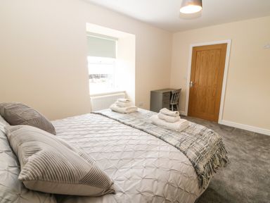 A bedroom with a bed featuring pillows and folded towels a window with a blind a wooden door and a small desk with a chair at Trewen in Botwnnog near Sarn Meyllteyrn