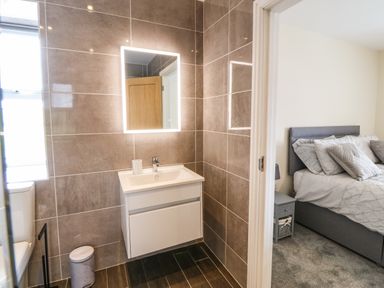 A bathroom with sink mirror and toilet visible next to a bedroom with bed and bedside table at Trewen in Botwnnog near Sarn Meyllteyrn