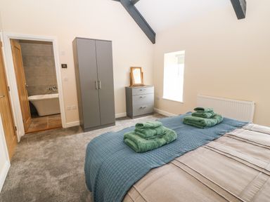A bedroom with a bed covered with a quilt and towels folded on top a wardrobe a chest of drawers with a mirror on top and an open door showing a bathroom with a bathtub at Trewen Botwnnog near Sarn Meyllteyrn