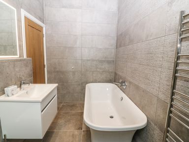A bathroom with a bathtub a white sink with mirror and a towel radiator at Trewen in Botwnnog near Sarn Meyllteyrn