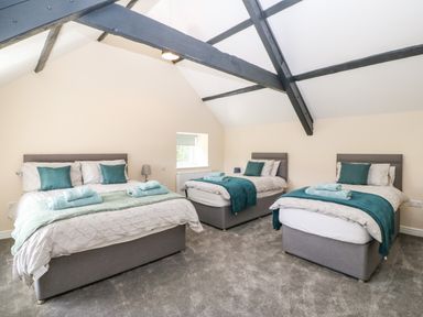A bedroom with three beds gray headboards teal blankets pillows and towels under exposed beams at Trewen in Botwnnog near Sarn Meyllteyrn