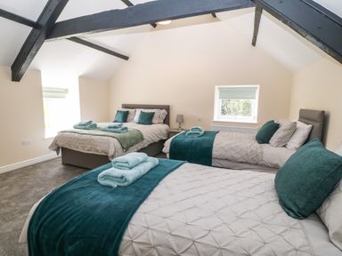 A bedroom with three beds two windows exposed ceiling beams and folded towels on the beds at Trewen in Botwnnog near Sarn Meyllteyrn