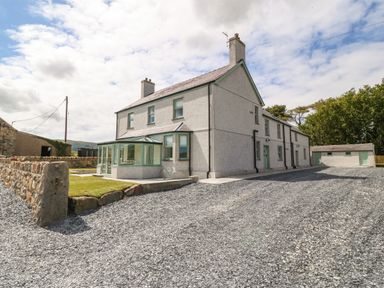 A two-story house with a conservatory and gravel driveway surrounded by a stone wall and trees at Trewen in Botwnnog near Sarn Meyllteyrn