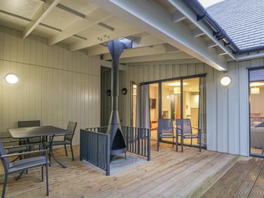 A covered outdoor patio with a black metal table and chairs and a chimney stove at Wildcat Lodge in Feshiebridge near Aviemore