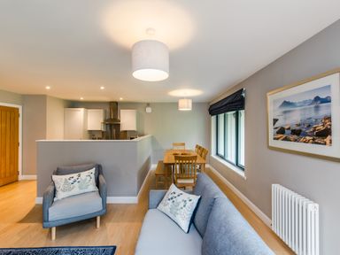An open plan living room and kitchen with a dining table chairs sofa armchair and framed landscape picture on the wall at Wildcat Lodge in Feshiebridge near Aviemore