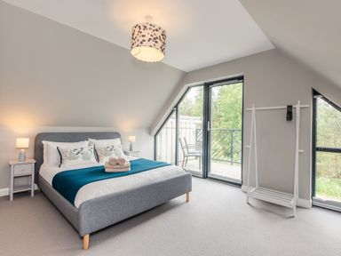 A bedroom with a bed table lamps a clothes rack and glass doors leading to a balcony at Wildcat Lodge in Feshiebridge near Aviemore
