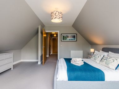 A bedroom with a bed with blue blanket and white pillows next to a nightstand with a lamp and a dresser against the wall at Wildcat Lodge in Feshiebridge near Aviemore