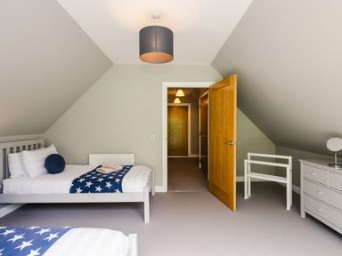 A bedroom with two single beds a dresser and an open wooden door at Wildcat Lodge in Feshiebridge near Aviemore