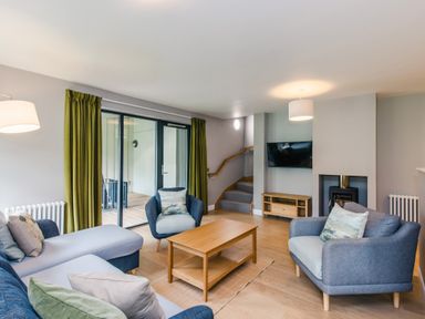 A living room with blue chairs a wooden coffee table TV and green curtains at Golden Eagle Lodge in Aviemore