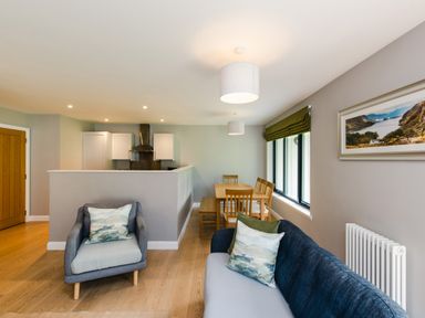 A living room with chairs and a sofa with cushions next to a dining table and kitchen at Golden Eagle Lodge in Aviemore