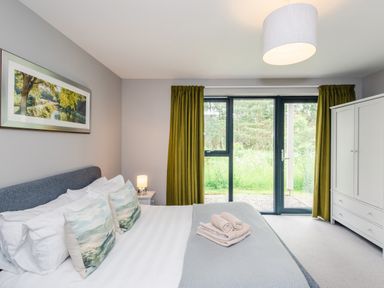 A bedroom with a double bed pillows bedside lamp wardrobe and green curtains at Golden Eagle Lodge in Aviemore