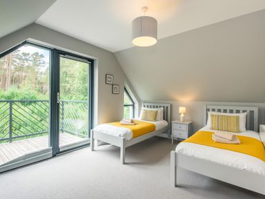 A bedroom with two single beds yellow bed runners nightstand lamp and balcony doors at Golden Eagle Lodge Aviemore