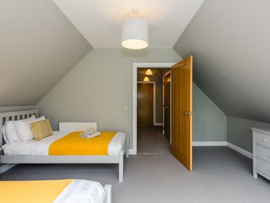 A bedroom with two single beds with yellow blankets a wooden door and a white dresser at Golden Eagle Lodge in Aviemore