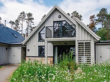 An exterior view of a two-story house with a balcony and wildflowers in front at Golden Eagle Lodge in Aviemore