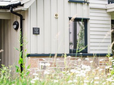 White wooden exterior wall of a building with a black sign reading Golden Eagle Lodge a window and wildflowers in front at Golden Eagle Lodge Aviemore
