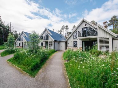 Three gray houses with black balconies surrounded by grass and flowers at Golden Eagle Lodge in Aviemore