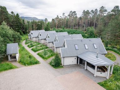 A row of cabins with gray roofs surrounded by trees and greenery at Golden Eagle Lodge in Aviemore