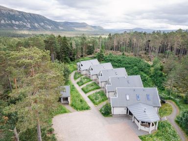 A row of houses with grey roofs surrounded by trees and mountains at Golden Eagle Lodge in Aviemore