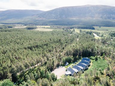 An aerial view of a forested area with a row of five houses and a mountain in the background at Golden Eagle Lodge in Aviemore