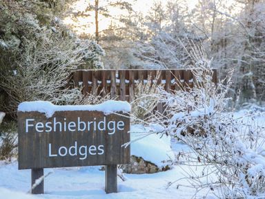 A sign for Feshiebridge Lodges surrounded by snow and trees