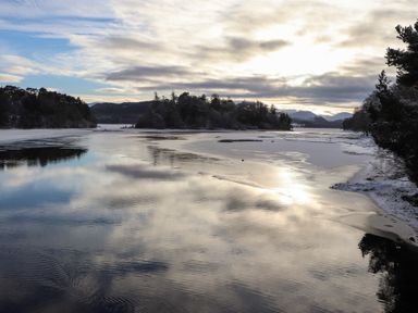 A lake with snow and trees along the shore at Golden Eagle Lodge in Aviemore